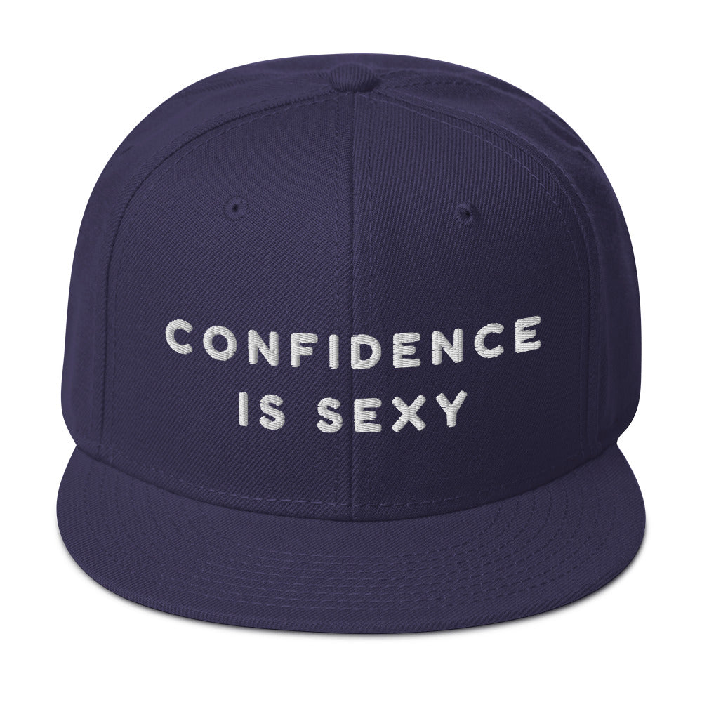Navy snapback hat with white embroidered text reading “CONFIDENCE IS SEXY”