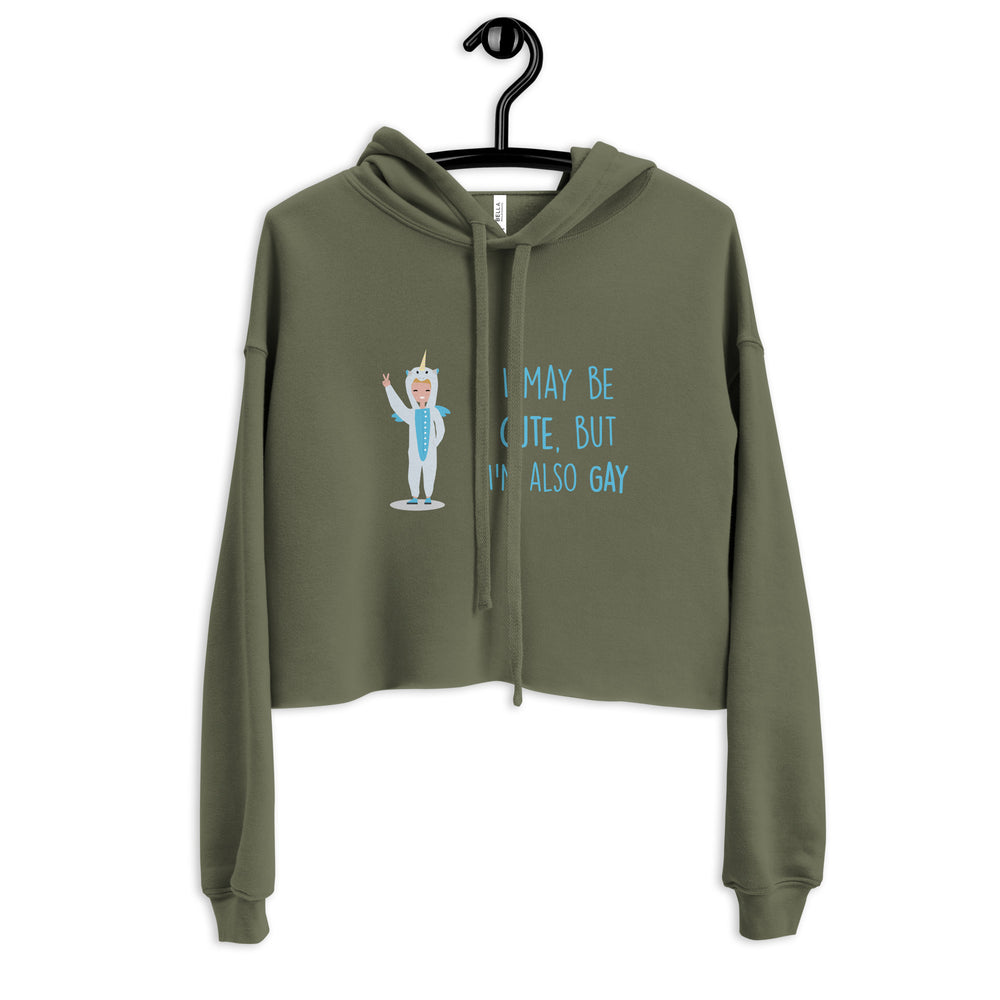 Front view of an olive green cropped hoodie with a unicorn graphic and blue text reading “I may be cute, but I’m also gay.”