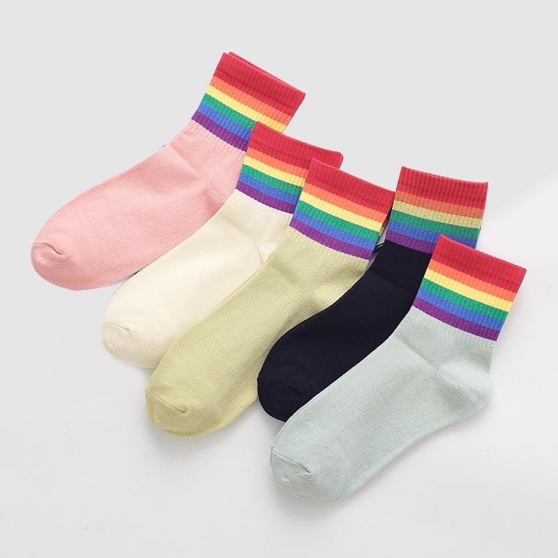 Five pastel crew socks with rainbow-striped cuffs arranged in a colorful flat lay