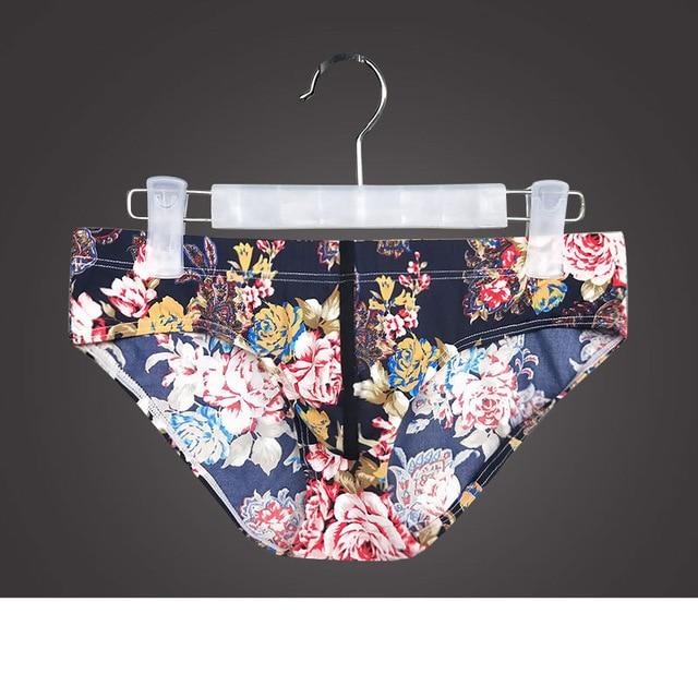 Dark floral-print briefs hanging from a clip hanger against a dark background
