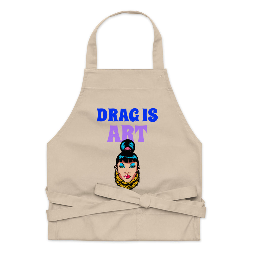 Front-facing beige apron reading “DRAG IS ART,” with a colorful drag-queen illustration