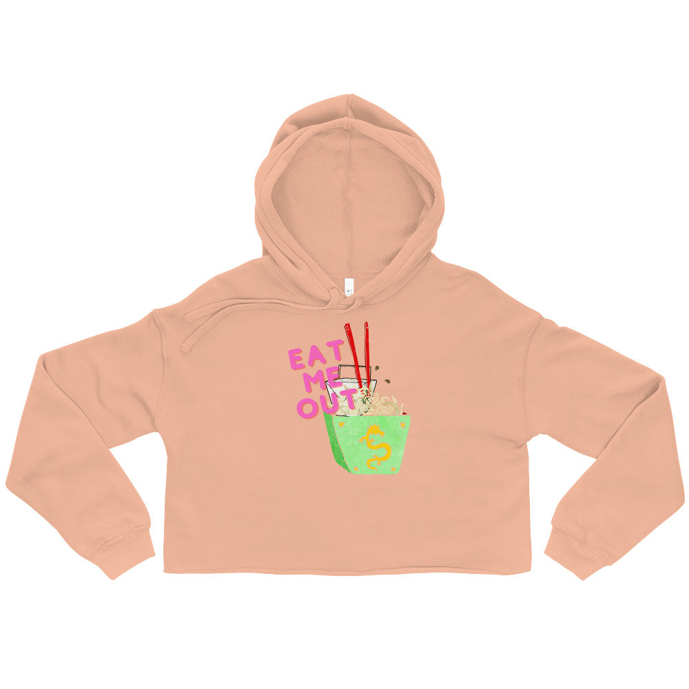Front view of a peach cropped hoodie reading “EAT ME OUT” beside a noodle bowl graphic