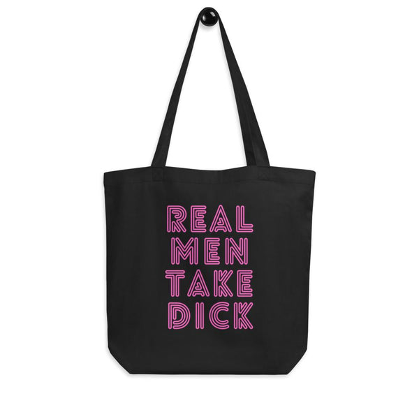 Black tote bag with pink outlined text reading “REAL MEN TAKE DICK”