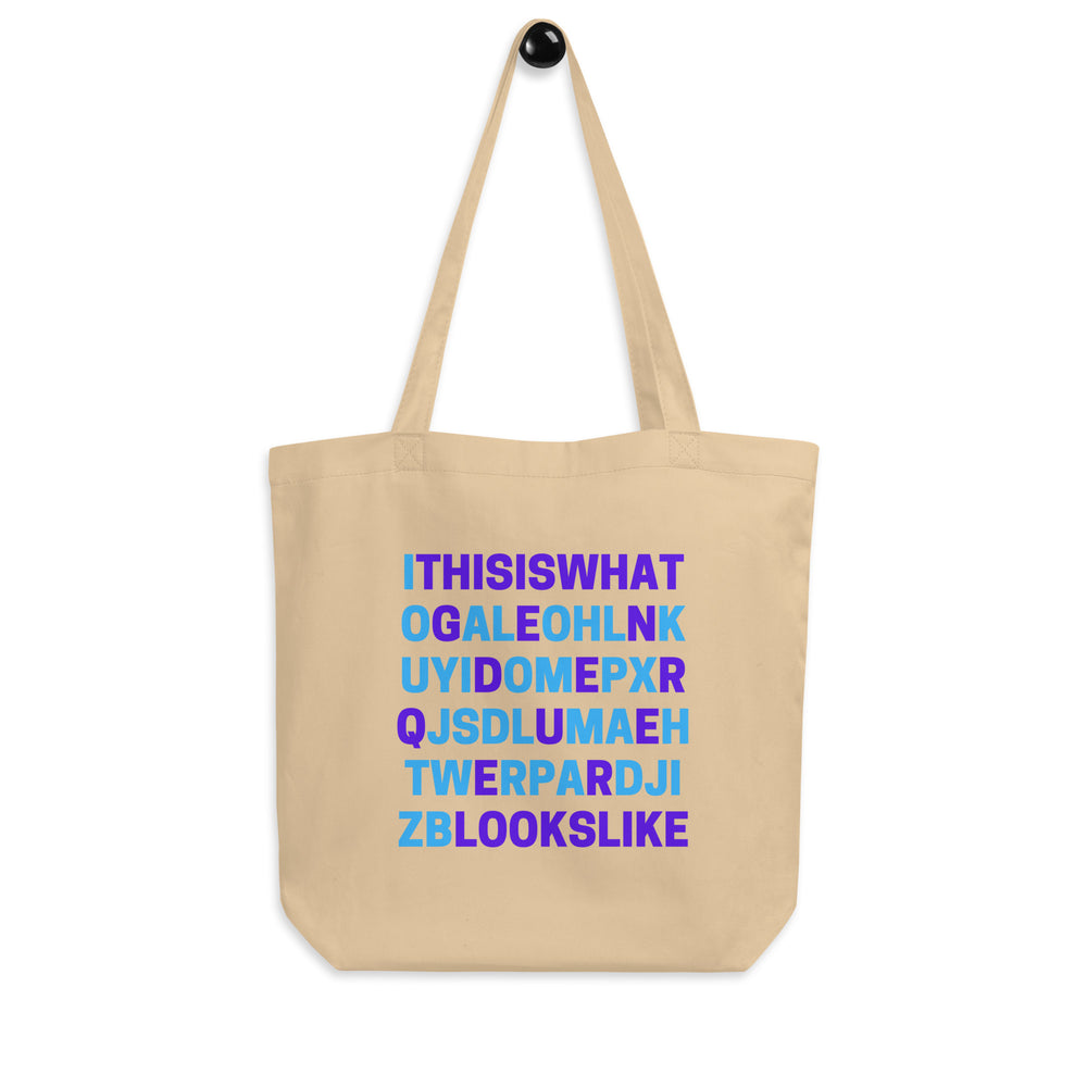 Front view of a beige tote bag reading “THIS IS WHAT GENDERQUEER LOOKS LIKE”
