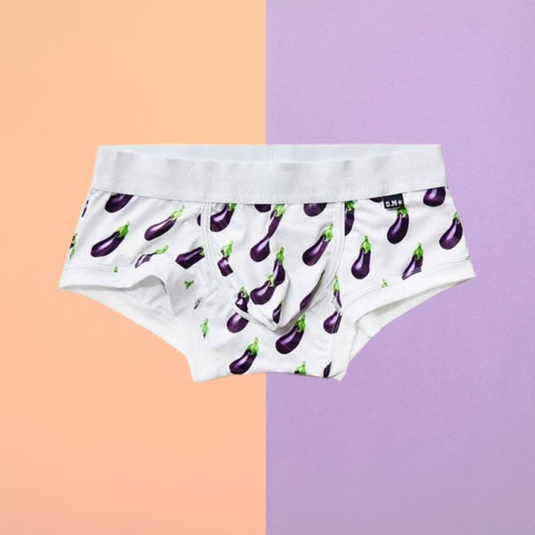 White boxer briefs covered in purple eggplant prints, shown against a peach and lavender background