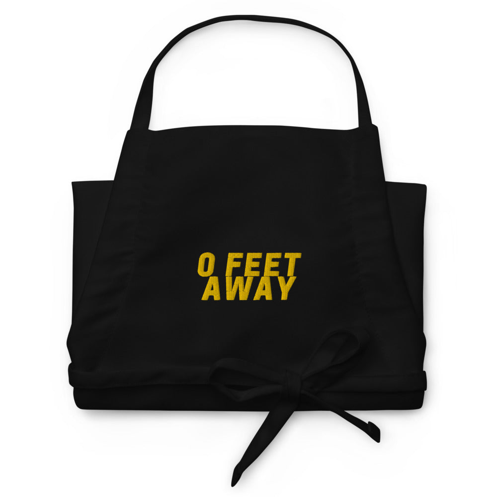 Front view of a black apron with yellow “0 FEET AWAY” text and waist ties
