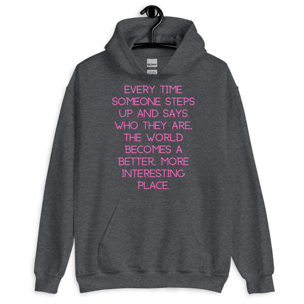 Front view of a dark gray hoodie with pink text: “Every time someone steps up and says who they are, the world becomes a b...