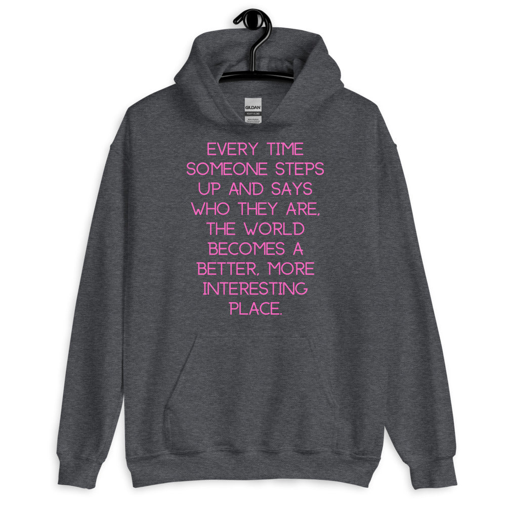 Front view of a dark gray hoodie with pink text: “Every time someone steps up and says who they are, the world becomes a b...