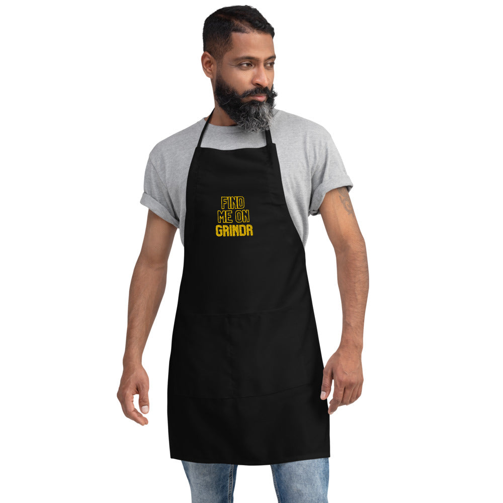 Front view of a person wearing a black apron embroidered with “FIND ME ON GRINDR” in yellow