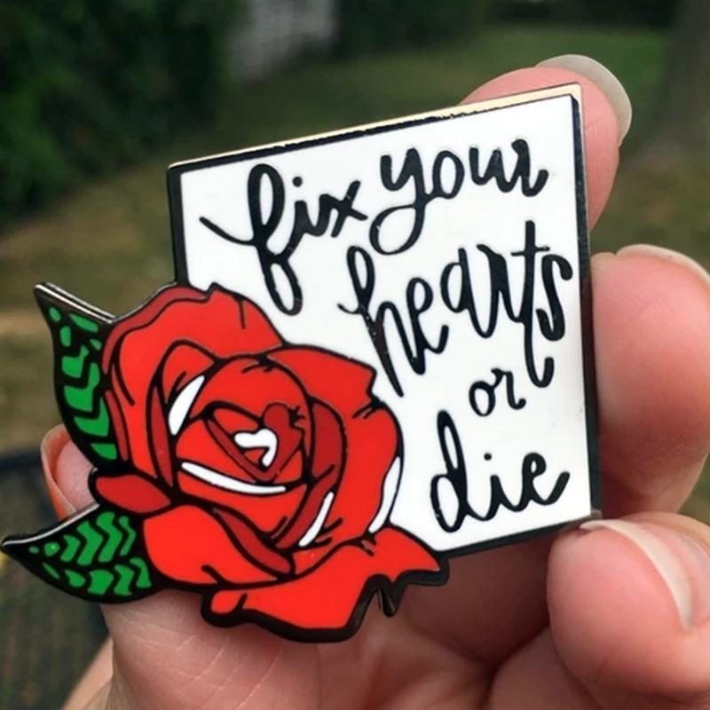 Enamel pin showing a red rose beside the words “fix your hearts or die”