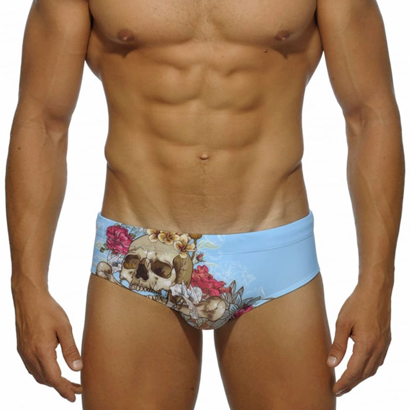 Model wearing light blue swim briefs with a floral skull print