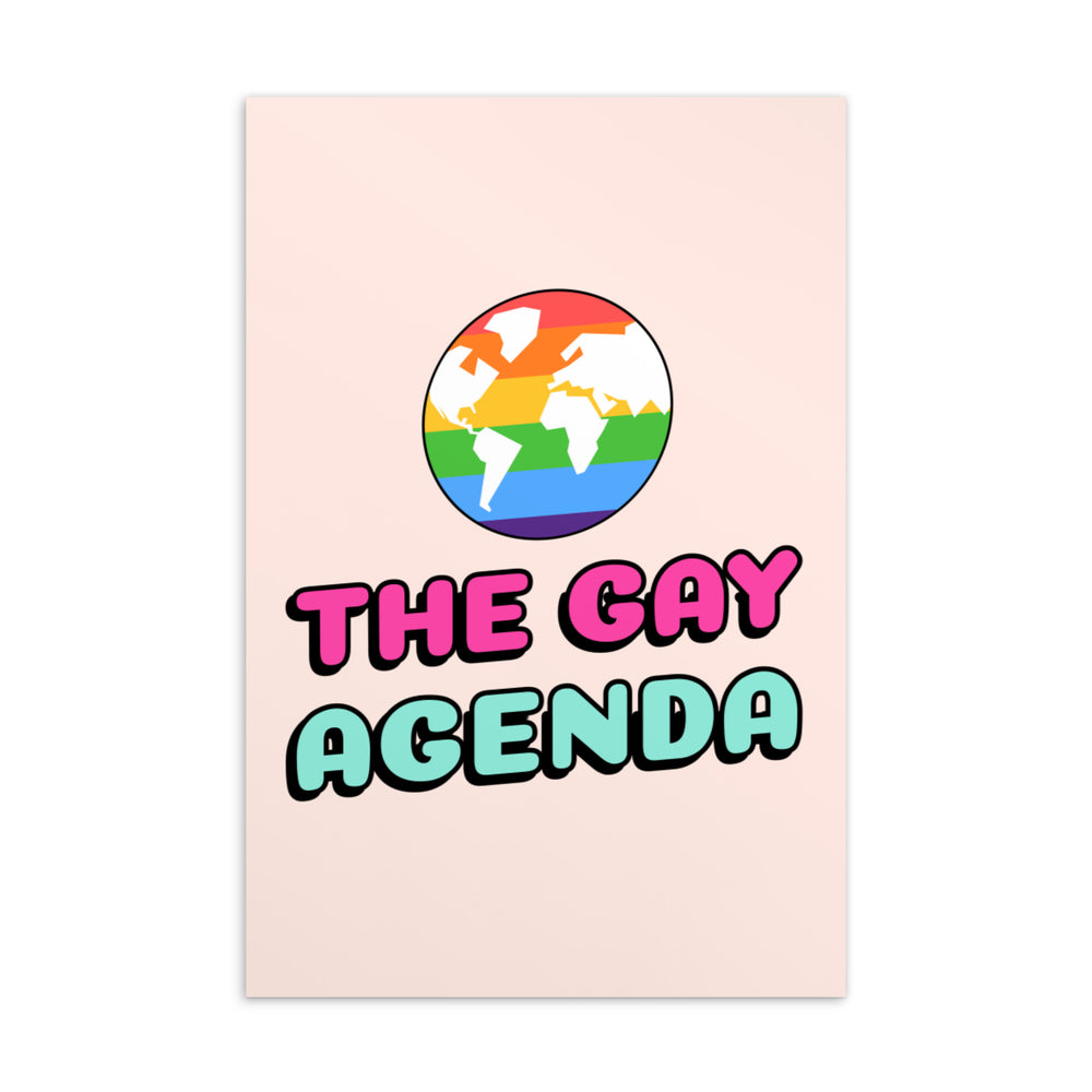 The Gay Agenda Postcard held by a smiling person in a gray tee with rainbow heart; pride stickers, queer postcards, sunny cafe.