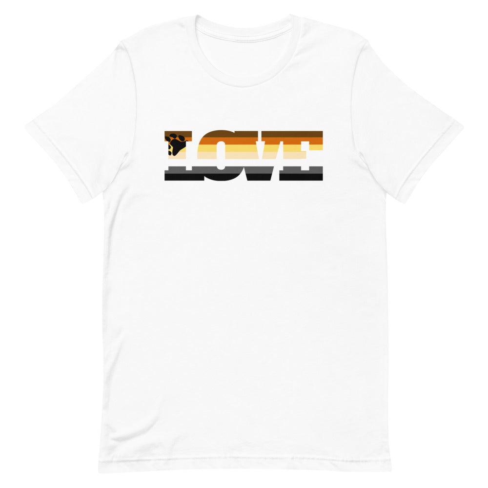 Gay Bear Love T-Shirt with a paw print as the “O” in LOVE, worn by a bearded man among vibrant flowers and greenery at sunset.
