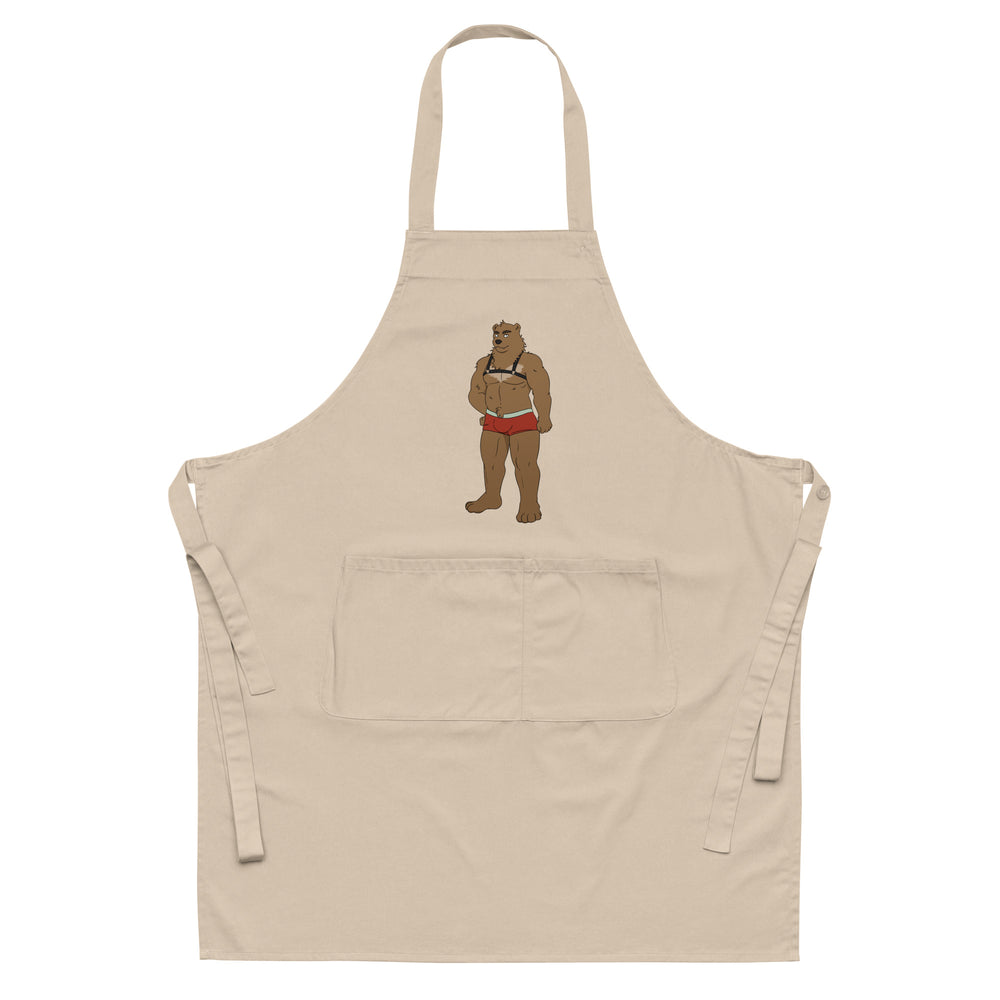 Front view of a beige apron with a cartoon bear in a harness and red briefs, plus a large pocket