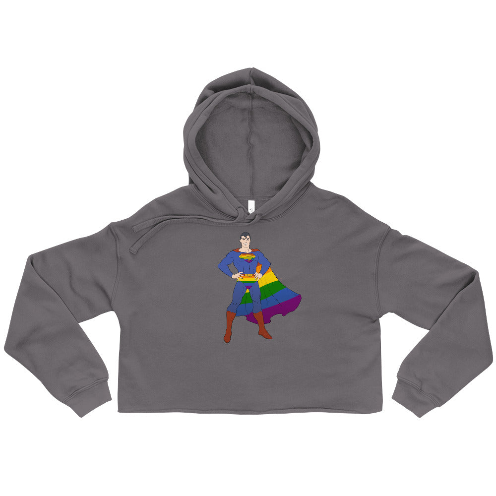 Gay Geek Crop Hoodie with superhero and rainbow flag graphics, worn by a young man in a dim, messy restroom, hands in pockets.