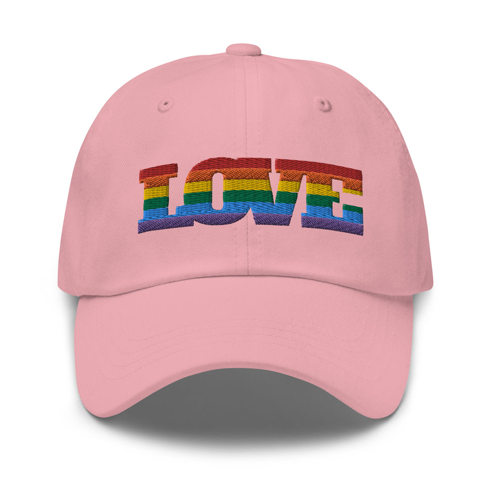 Pink pride cap with "LOVE" stitched in rainbow colors, worn by a smiling queer person with short hair, earrings, and silver ring.