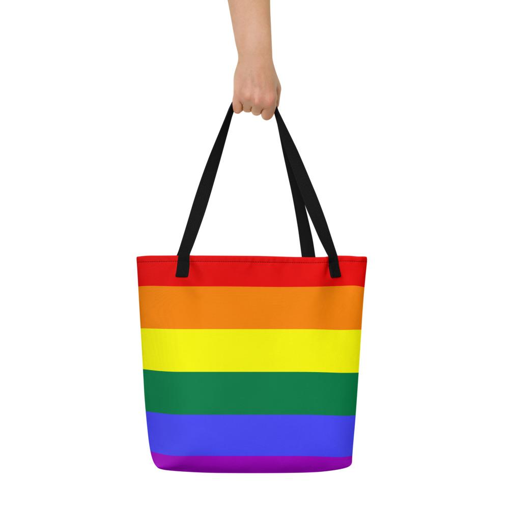 Rainbow-striped tote bag with black handles, held up by one hand against a white background