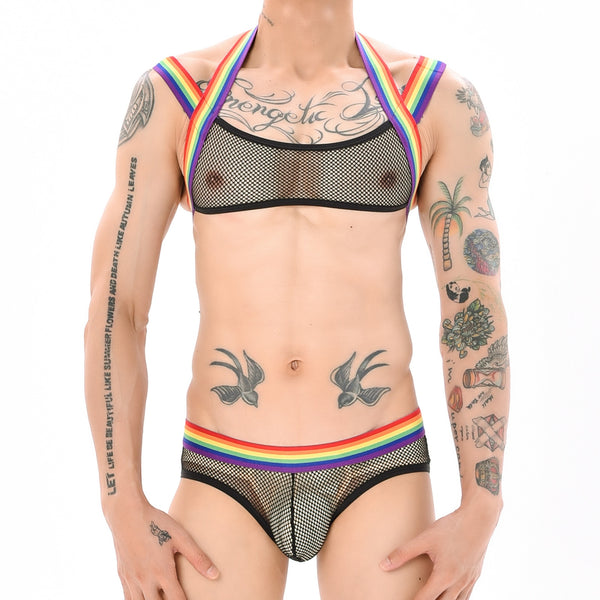 Front-facing model wearing a black mesh harness and briefs with rainbow Pride trim