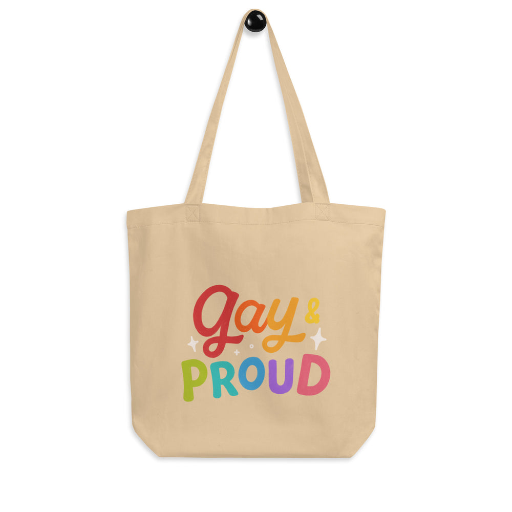 Front view of a beige tote bag reading “Gay & Proud” in multicolored letters