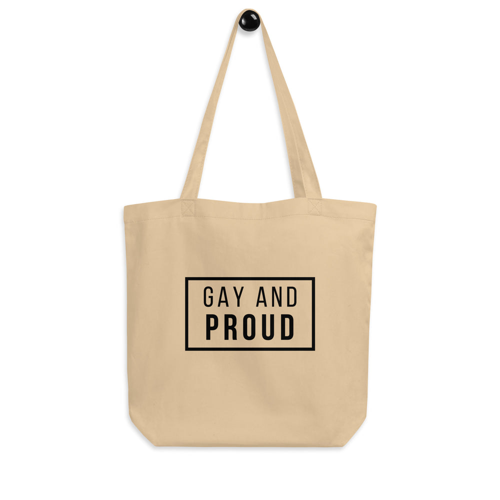 Front view of a beige tote bag reading “GAY AND PROUD” in black inside a rectangle