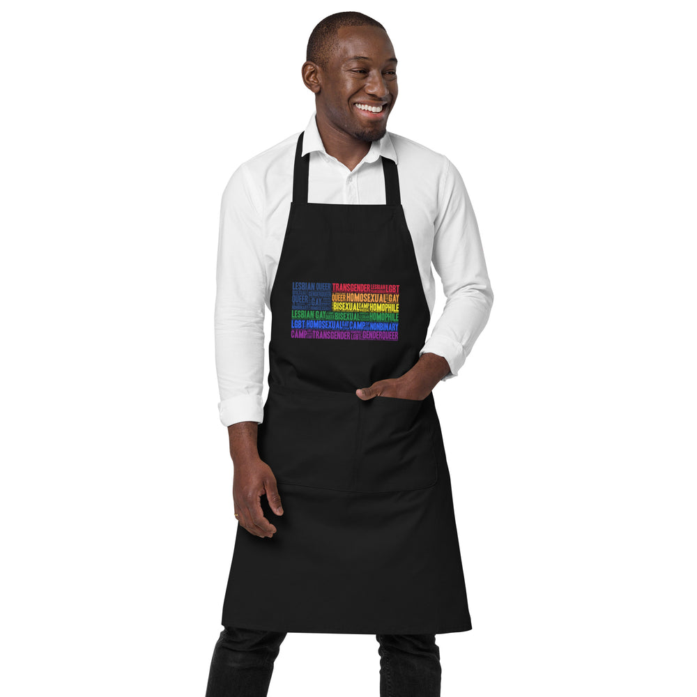 Person wearing Black apron with colorful LGBTQ+ word collage; gay Pride organic cotton apron with “Gay USA” design