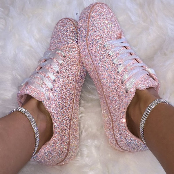 A person wears matching pink glitter lace-up sneakers with white laces and rhinestone ankle straps