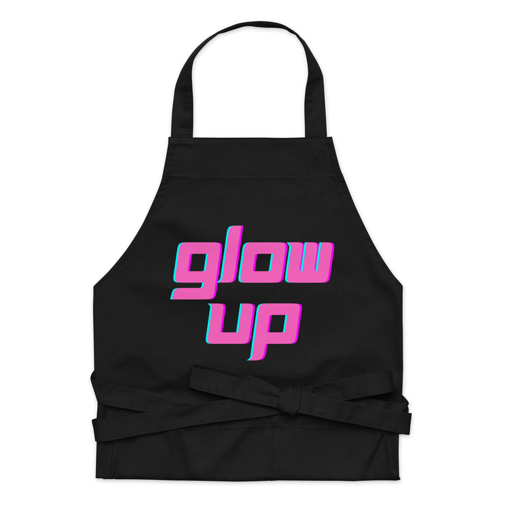 Front view of a black apron with pink and turquoise “glow up” lettering and waist ties
