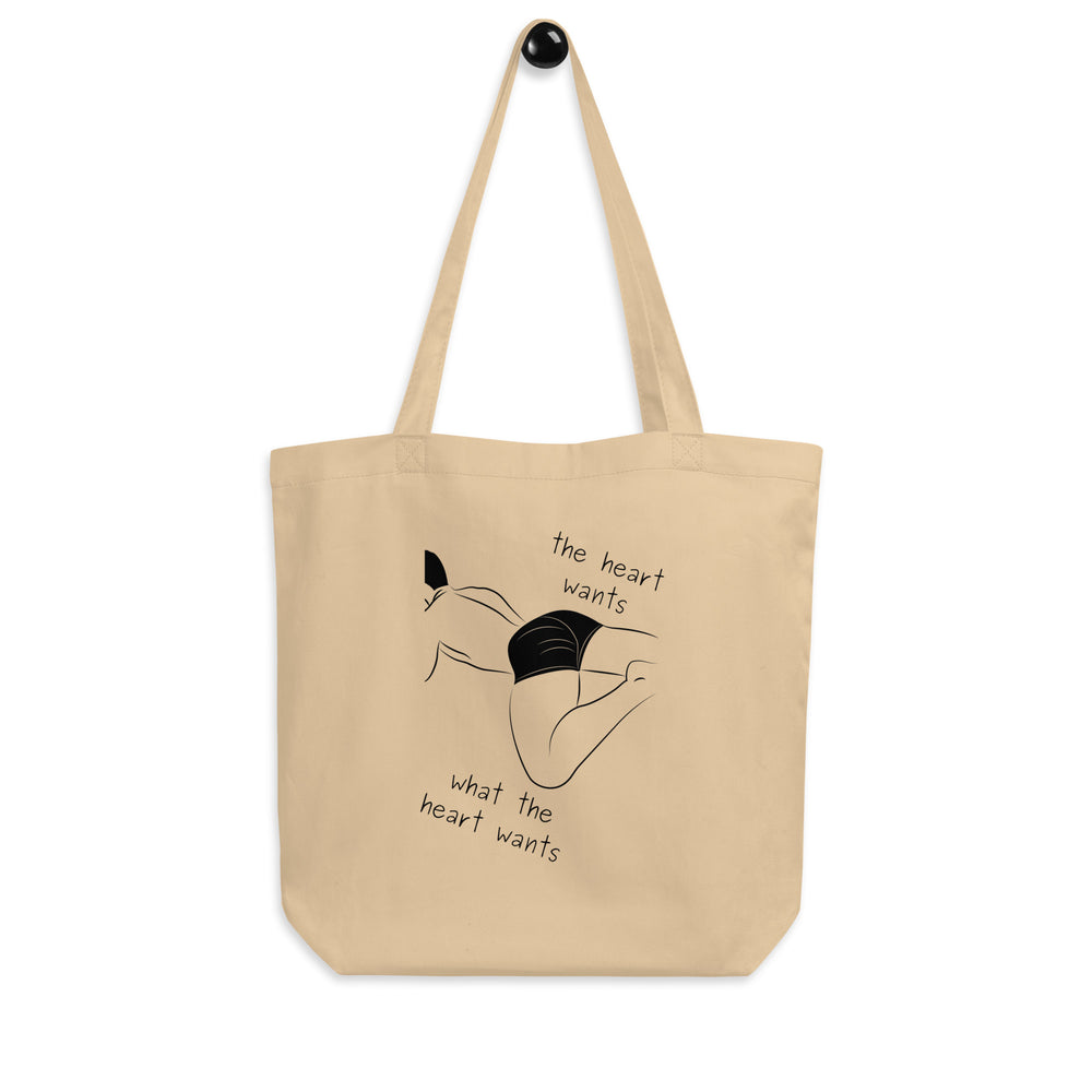 Front view of a beige tote bag with a black line drawing and “the heart wants what the heart wants” text