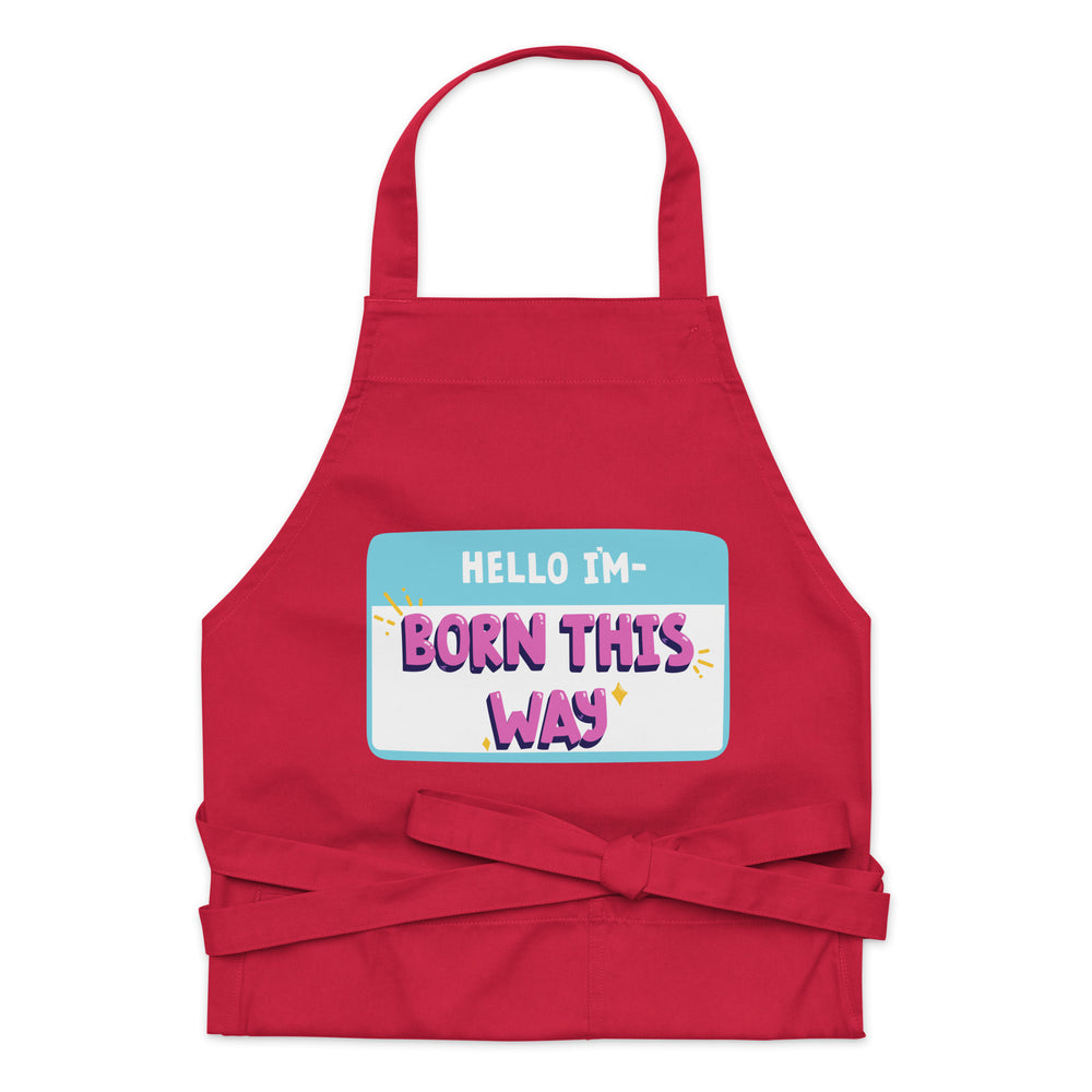 Front-facing red apron with a neck loop, waist ties, and “HELLO I'M—BORN THIS WAY” graphic
