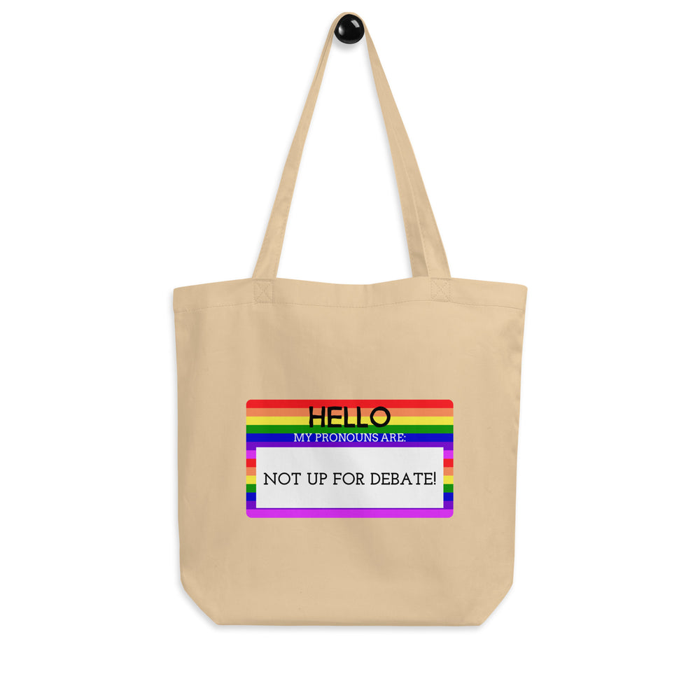 Front-facing beige tote bag with rainbow-bordered text reading “HELLO MY PRONOUNS ARE: NOT UP FOR DEBATE!”