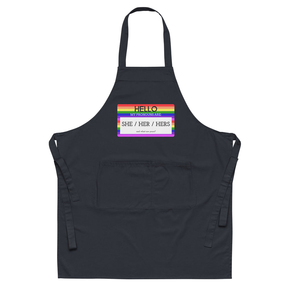 Black apron with rainbow-bordered badge reading “HELLO MY PRONOUNS ARE: SHE / HER / HERS”