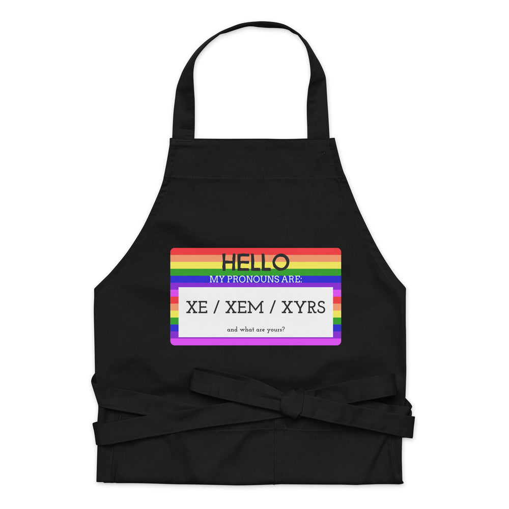 Black apron with rainbow-striped panel reading “Hello, my pronouns are: xe / xem / xyrs”