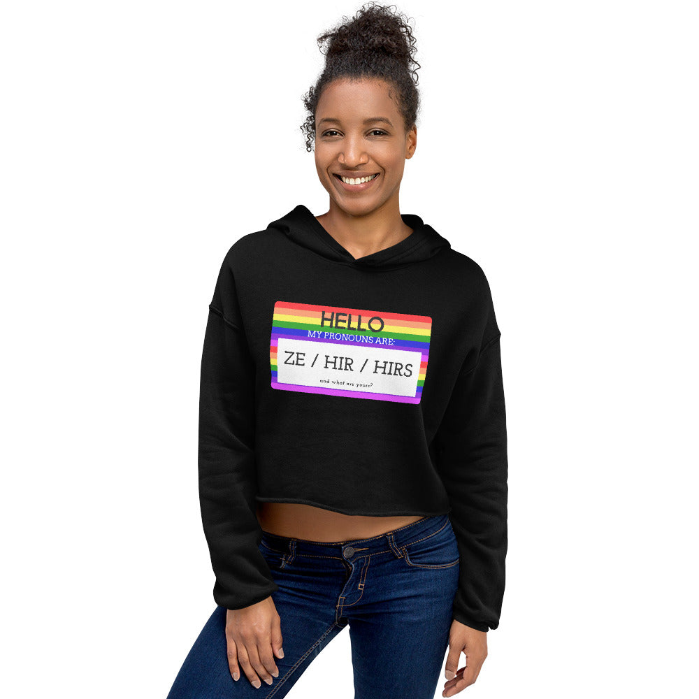 Model wearing a black cropped hoodie with a rainbow pronoun badge reading “ZE / HIR / HIRS”