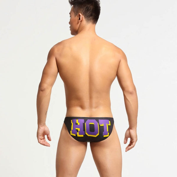 Rear view of a model wearing black briefs with large purple and yellow HOT lettering