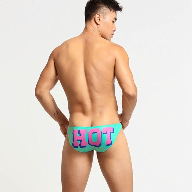 Rear view of a model wearing turquoise briefs with large pink-and-purple “HOT” lettering