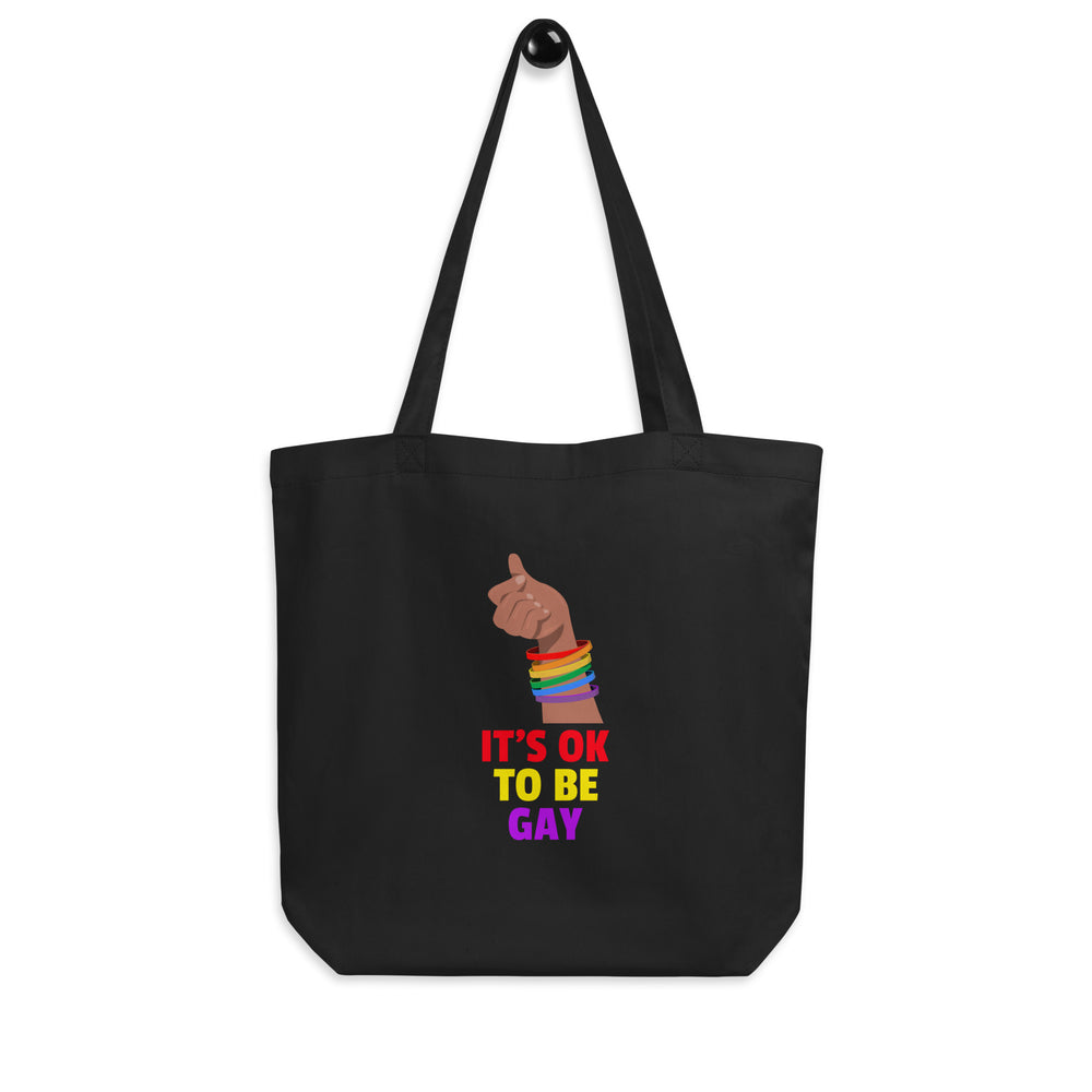 Front view of a black tote bag with a rainbow-braceleted fist and “IT’S OK TO BE GAY” text