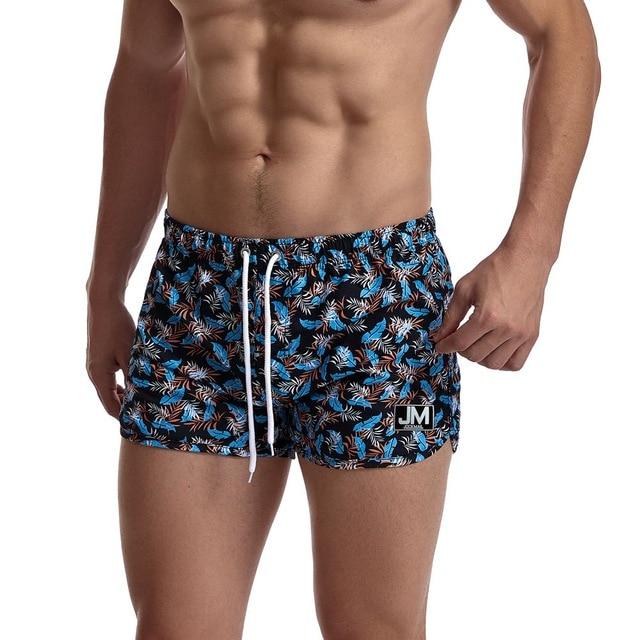Blue leaf-print board shorts with white drawstring and JM logo patch, shown on a model
