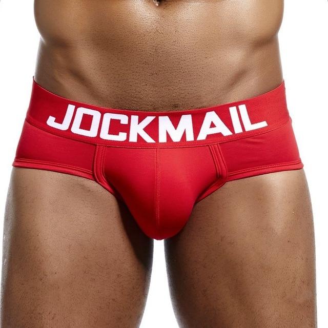 Red Jockmail low-rise brief with a wide white logo waistband, modeled from the front