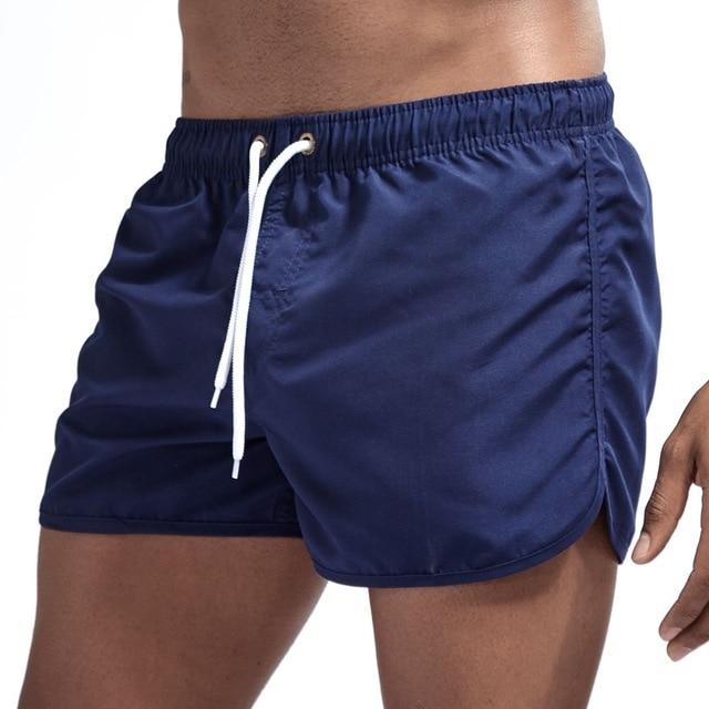 Navy blue swim shorts with elastic waistband, white drawstring, side pockets and curved hems