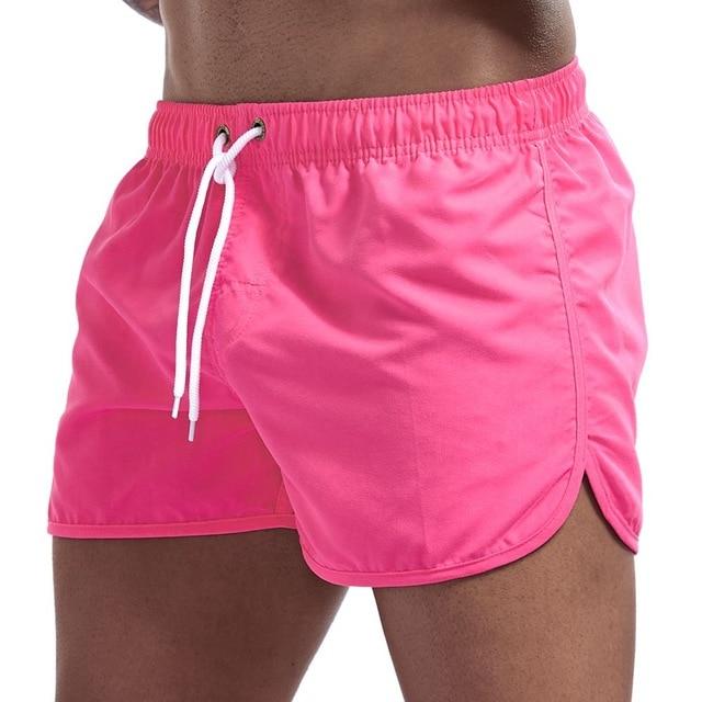 Bright pink swim shorts with white drawstring and curved split hems