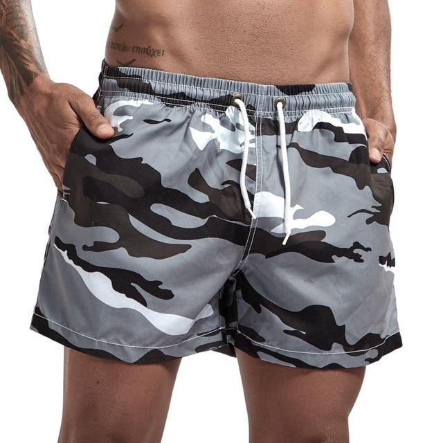 Model wearing gray, black, and white camouflage swim shorts with drawstring waist and side pockets
