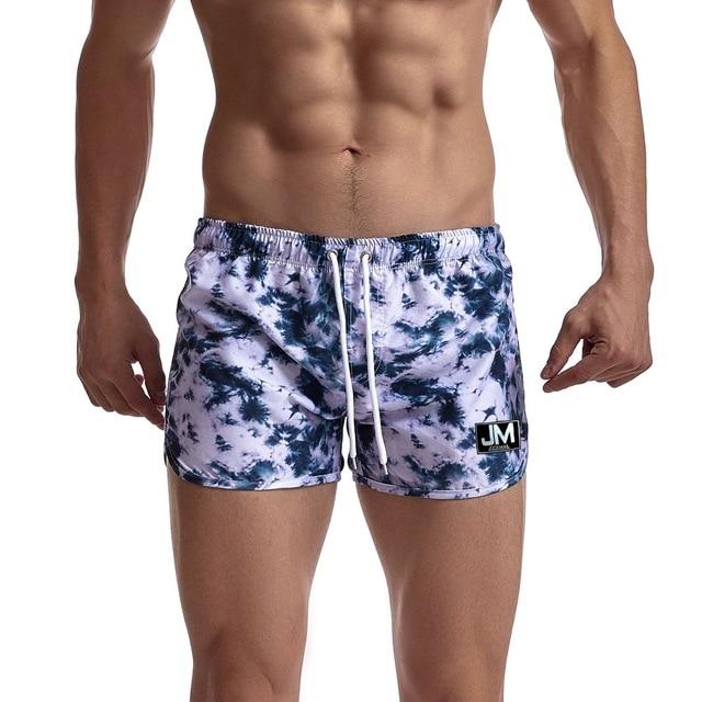 Model wearing purple and black acid-wash board shorts with a white drawstring and JM patch