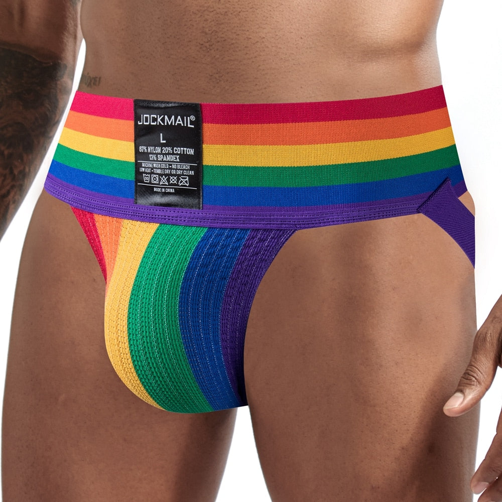 Front close-up of a model wearing a rainbow-striped mesh jockstrap with purple trim