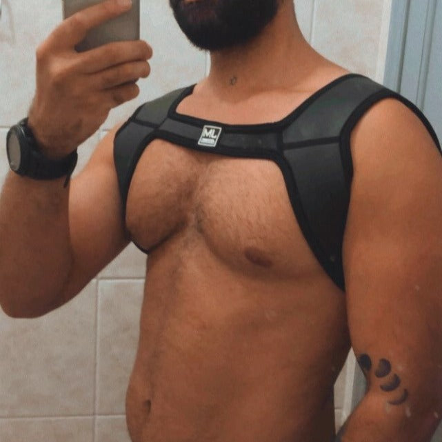 Model wearing a black neoprene chest harness with broad shoulder straps and a center logo