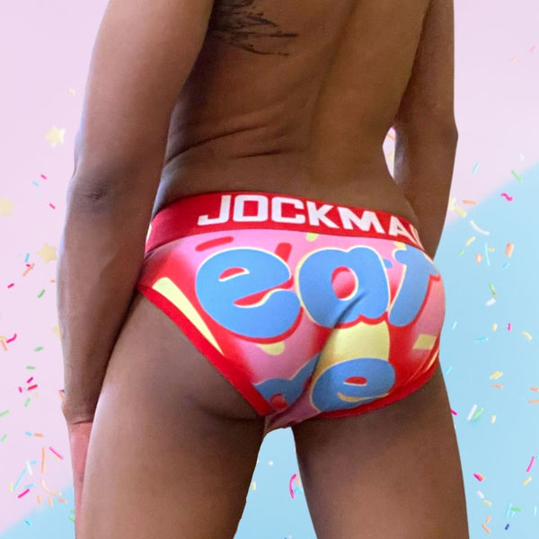 Rear view of a model wearing colorful pink briefs with blue lettering and a red JOCKMAIL waistband
