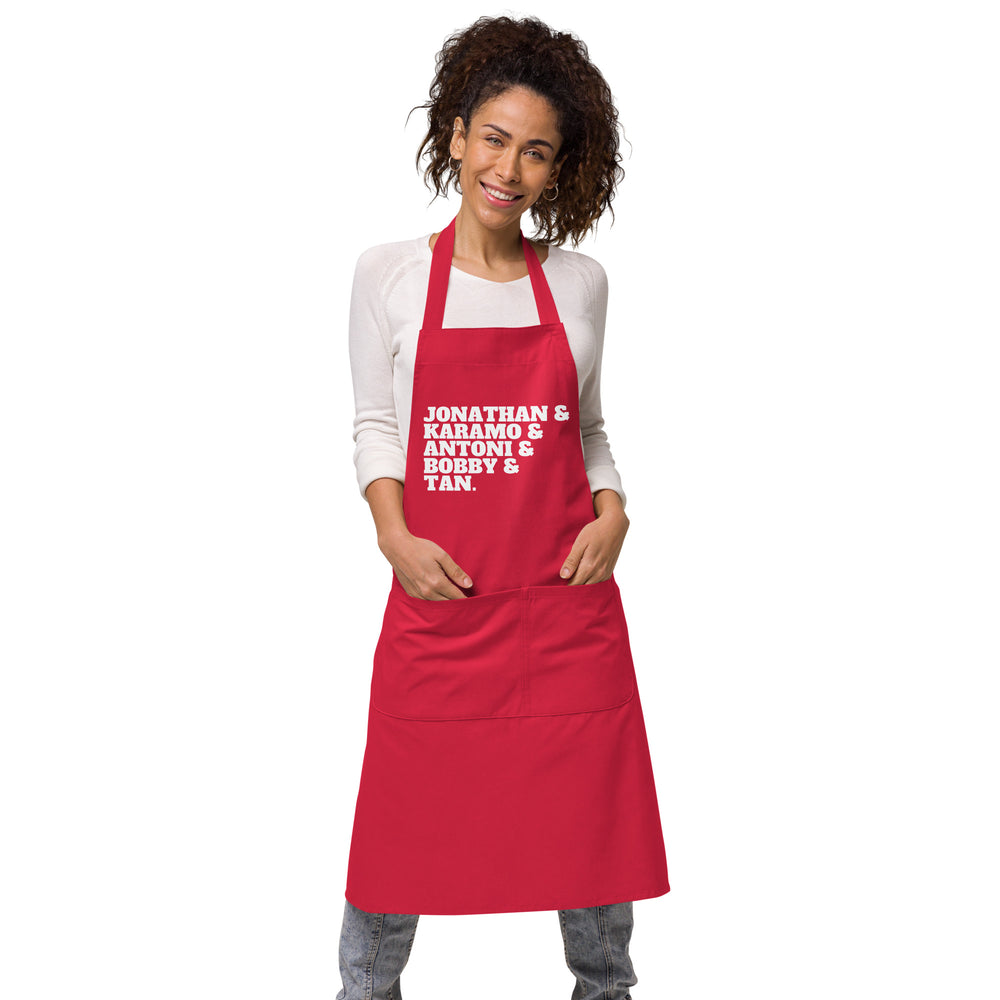 Front-view model wearing a red apron reading “JONATHAN & KARAMO & ANTONI & BOBBY & TAN.”