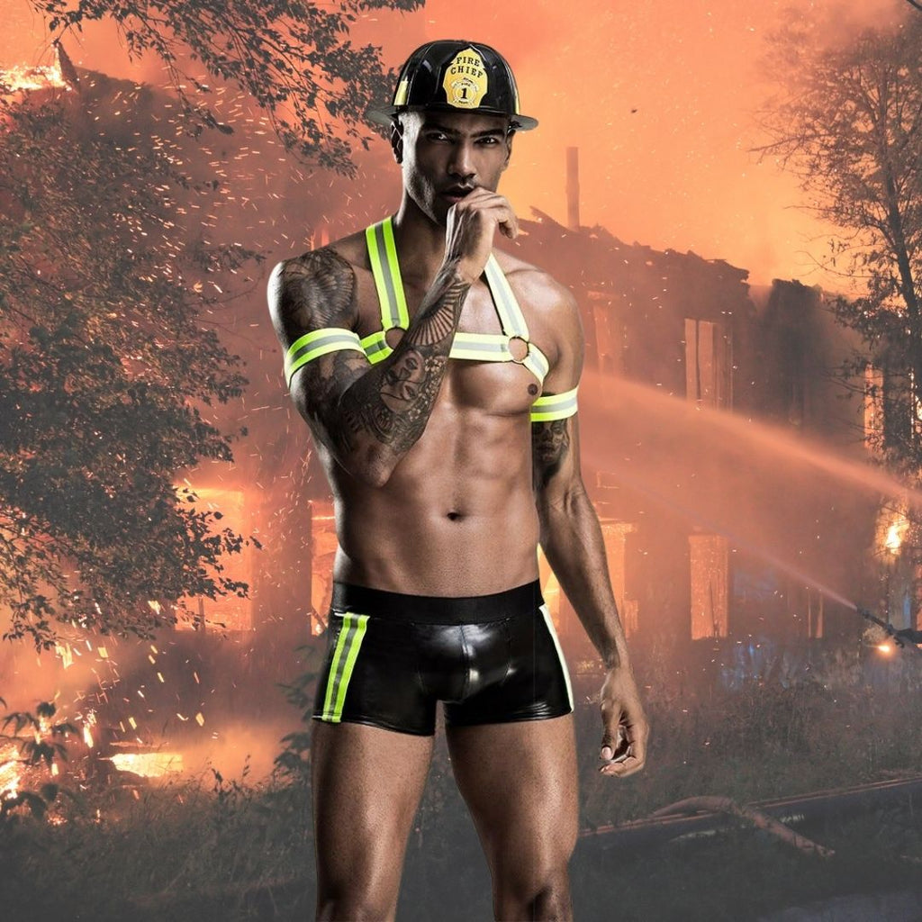 Model wearing a black fireman costume with neon yellow harness straps, shorts, and fire chief helmet