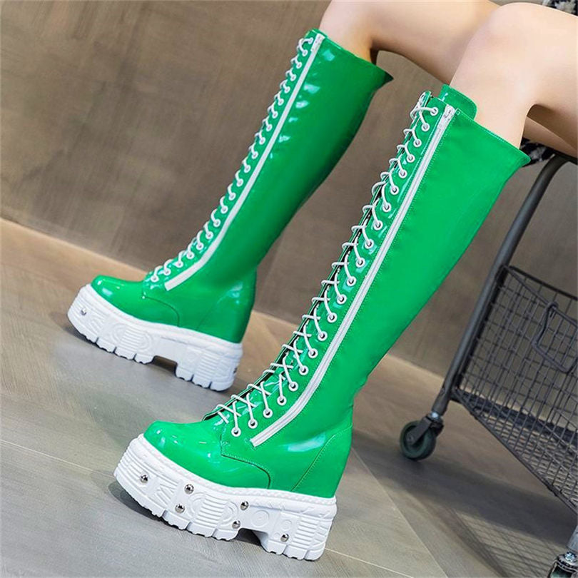 Bright green knee-high platform wedge boots with white laces and zippers, shown on a seated model