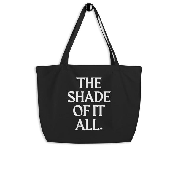 Black large tote bag with white “THE SHADE OF IT ALL.” slogan and long shoulder straps