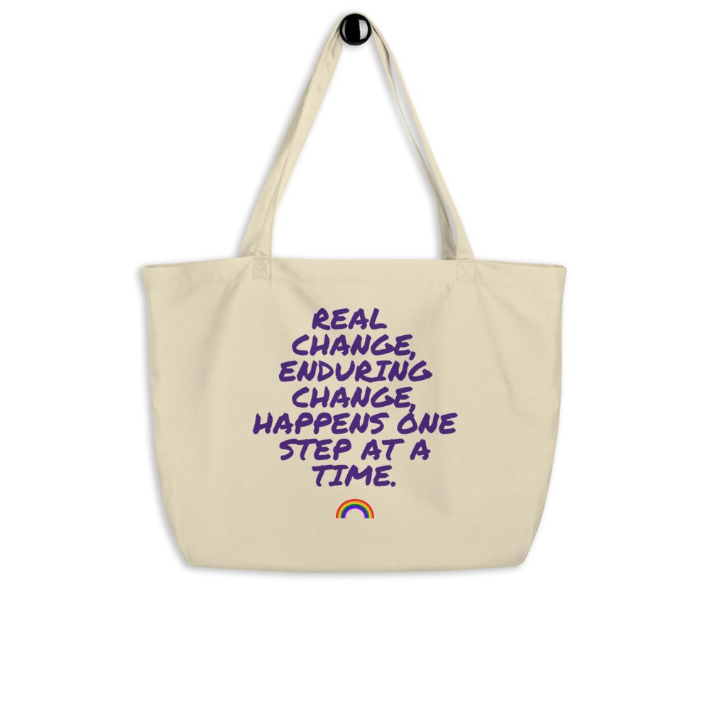 Cream organic tote bag with purple “Real Change, Enduring Change...” slogan and rainbow graphic